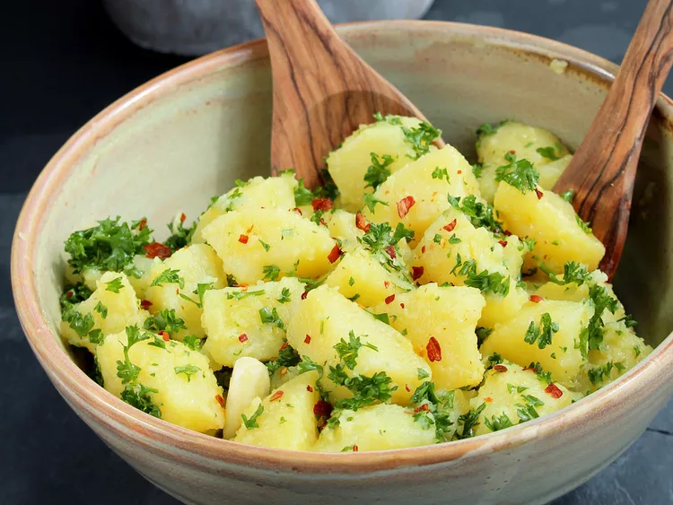 a bowl of potato salad with two wooden spoons in it