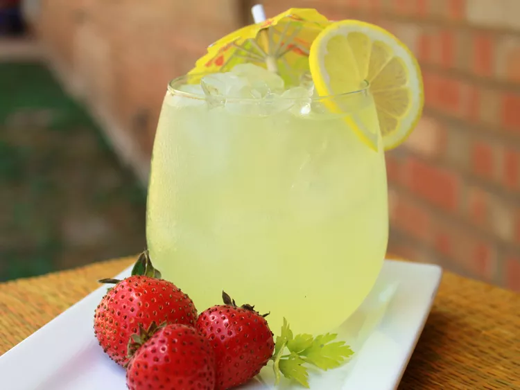 a glass of lemonade with a small umbrella and a lemon slice in it